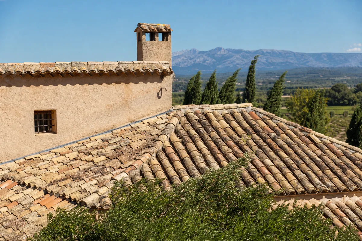 Toiture en tuiles canal patinées d’une bastide provençale sous le soleil